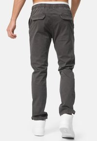 Pantalones de chándal grises con cintura elástica, bolsillos laterales y bolsillos traseros con botón, combinados con zapatillas blancas.