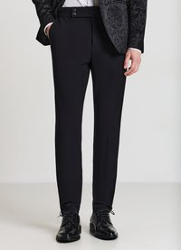 Schwarze, maßgeschneiderte Hosen mit schmaler Passform, glatter Textur, zwei vorderen Taschen und einem Bund mit zwei Knöpfen. Kombiniert mit glänzenden schwarzen Schuhen.