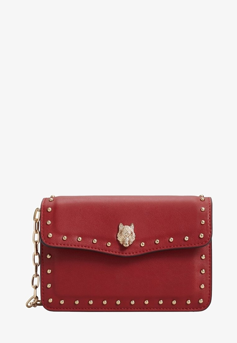 Červená kožená crossbody taška se zlatými hrotovými akcenty a dekoračním uzávěrem ve tvaru vlčí hlavy. Klopový design s řetízkem. Hladký povrch.