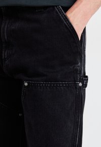Black denim pants with a slim fit, featuring a side pocket and silver hardware. The fabric has a soft texture and subtle weaving pattern.