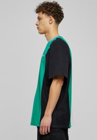 Krāsu blokēta T-krekls ar zaļu augšējo daļu un melnu apakšējo daļu, īsām piedurknēm un brīvu piegriezumu. Izgatavots no mīksta kokvilnas auduma.