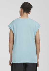 Light blue cotton t-shirt with rolled short sleeves, loose fit, and a rounded neckline. Smooth texture, minimalist design.