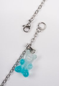 Lanț din metal argintiu cu un farmec de ursuleț din gumă transparent și albastru, având o textură fină și un sistem de prindere tip lobster.