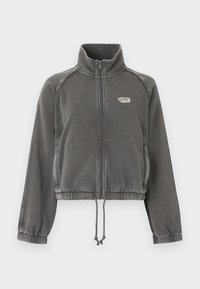 Σκούρα γκρι φλις μπουφάν με φερμουάρ, ψηλό γιακά, ελαστικές μανσέτες, ρυθμιζόμενο στρίφωμα με κορδόνι και μικρό λευκό λογότυπο στο αριστερό στήθος.