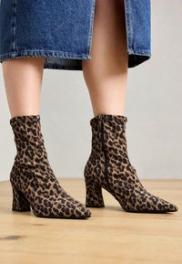 Stivaletti alla caviglia con stampa leopardata in morbido tessuto, punta appuntita, tacco quadrato di media altezza e dettaglio con zip laterale.