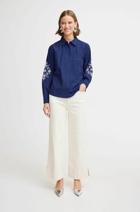 Navy button-up shirt with floral embroidery on sleeves, paired with white wide-leg trousers and silver pointed-toe heels.