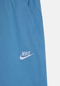 Světle modré Nike tepláky s hladkou strukturou, elastickým pasem, bočními kapsami a bílým vyšitým logem na levém stehně.