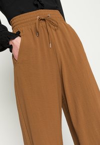 Calças de jogging leves e texturizadas, na cor castanha, com cintura elástica, detalhe de cordão e bolsos laterais.