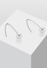 Pendientes de plata con un diseño de gancho curvado y una sola perla blanca redonda. Las perlas tienen una textura suave y un acabado brillante.