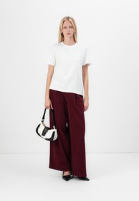 Chemise blanche à manches courtes, pantalon large bordeaux à coupe ample, chaussures noires à bouts pointus et petit sac à main noir et blanc.