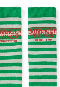 Calze a righe verdi e grigio chiaro con la scritta "STRANGER THINGS" e "BENETTON" in rosso, con bordo a costine e texture morbida.