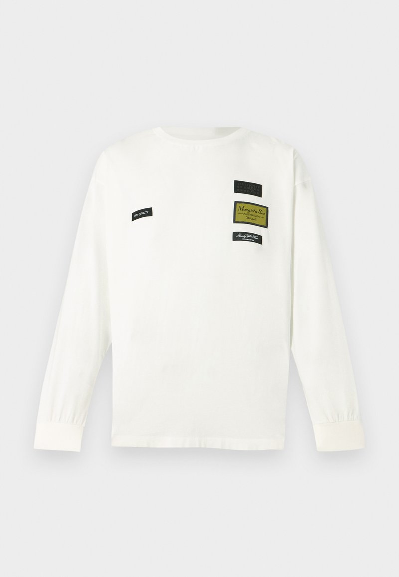 Camicia bianca a maniche lunghe con collo rotondo, caratterizzata da numerose toppe di tessuto in nero e verde con dettagli testuali. Realizzata in morbido cotone.