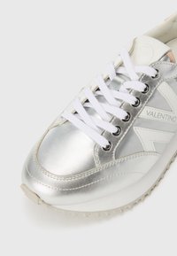Silberner Sneaker mit metallisch glänzendem Lederobermaterial, weißen Schnürsenkeln und Gummisohle. Verfügt über ein Logo an der Seite und eine glatte Textur.