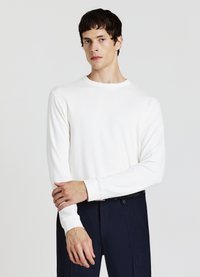 Weißes Langarmshirt mit Rundhalsausschnitt und gerippten Bündchen, kombiniert mit dunkler Hose. Glatter Stoff mit minimalistischem Design.