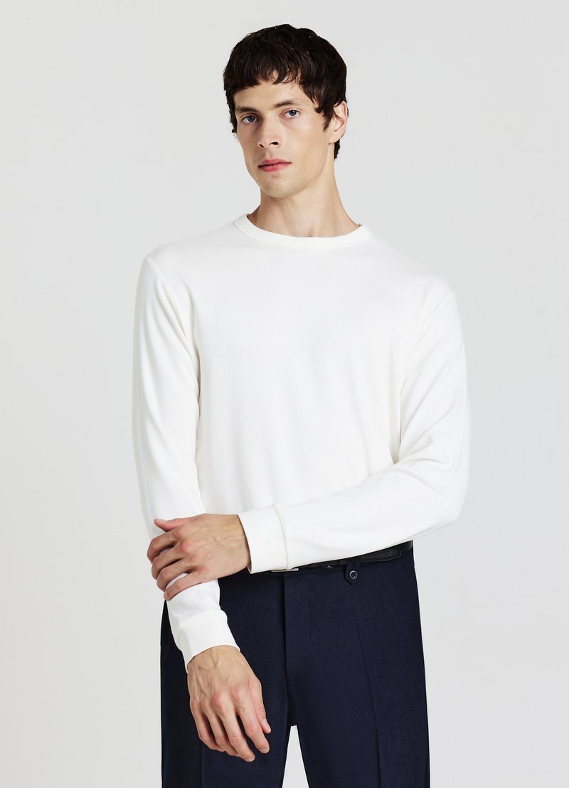 Weißes Langarmshirt mit Rundhalsausschnitt und gerippten Bündchen, kombiniert mit dunkler Hose. Glatter Stoff mit minimalistischem Design.