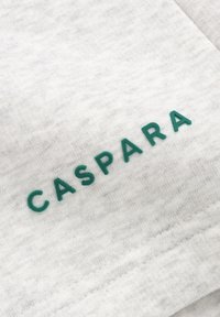 Bomullgenser i lys grå med strukturert overflate, med hevet grønn tekst "CASPARA" foran.