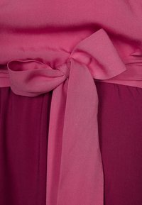 Fuksia mekko, jossa on satiinikangas, leveä, kuvioitu vyötärö ja edessä solmittu nauha, sekoittaen vaaleanpunaisen ja tumman burgundin sävyjä.