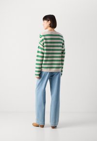 Maglione a righe verde e beige, con maniche lunghe e vestibilità rilassata, abbinato a jeans a gamba larga blu chiaro e scarpe con tacco in legno beige.