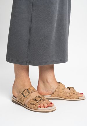 Voeten met kurk-gestructureerde slippers met twee gouden gespen en rood gelakte teennagels, gecombineerd met een grijze rok.