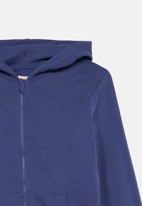 Tume sinine lukuga jaki, valmistatud pehmest kangast, millel on reguleeritav kapuuts ja ees olevad taskud. Sile tekstuur vähese detailikäsitlusega.