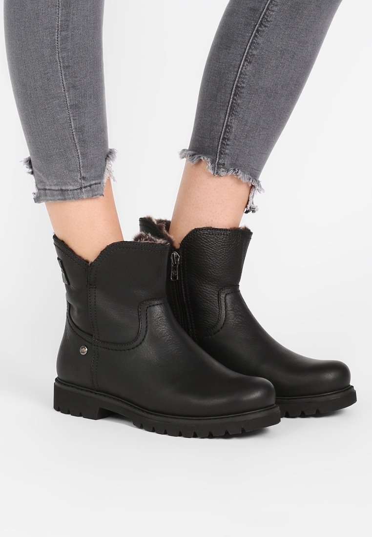 Bottes basses en cuir noir avec doublure en fourrure, fermeture éclair latérale, portées avec un jean skinny gris à ourlet effiloché.