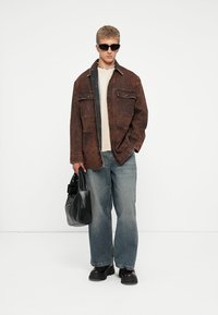 Brown denim jacket over a beige sweater, paired with light blue wide-leg jeans. Accessorized with black sunglasses and a sleek black bag.
