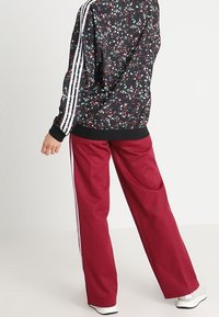 Chaqueta negra con estampado floral y rayas blancas en las mangas, combinada con pantalones holgados de color granate. Cuenta con tela texturizada y puños elásticos.