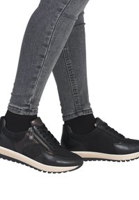 Sneakers neri in pelle con finitura testurizzata, dotati di una cerniera laterale e di una suola beige a contrasto. Indossati con jeans skinny grigi.