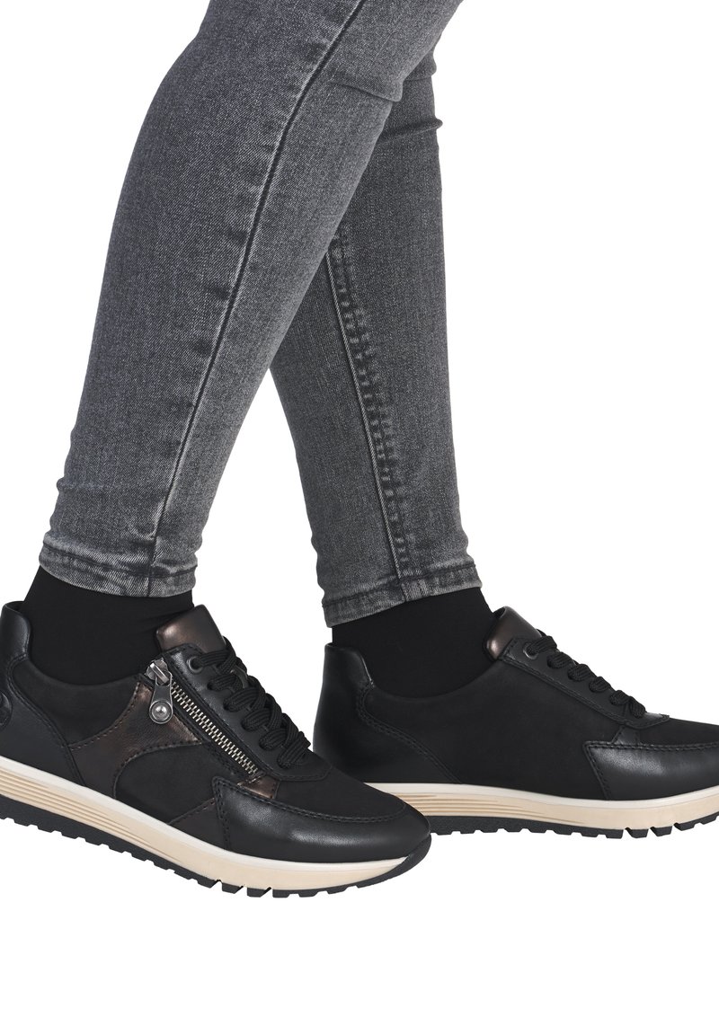 Sneakers neri in pelle con finitura testurizzata, dotati di una cerniera laterale e di una suola beige a contrasto. Indossati con jeans skinny grigi.