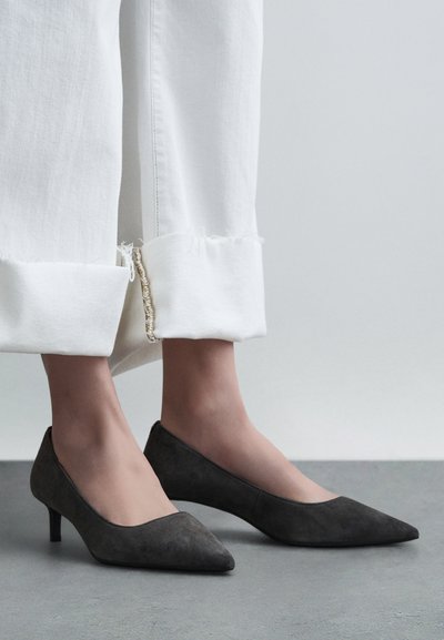 Escarpins pointus en suède gris avec un petit talon, associés à un pantalon blanc à ourlet effiloché, présentant un design simple et épuré.