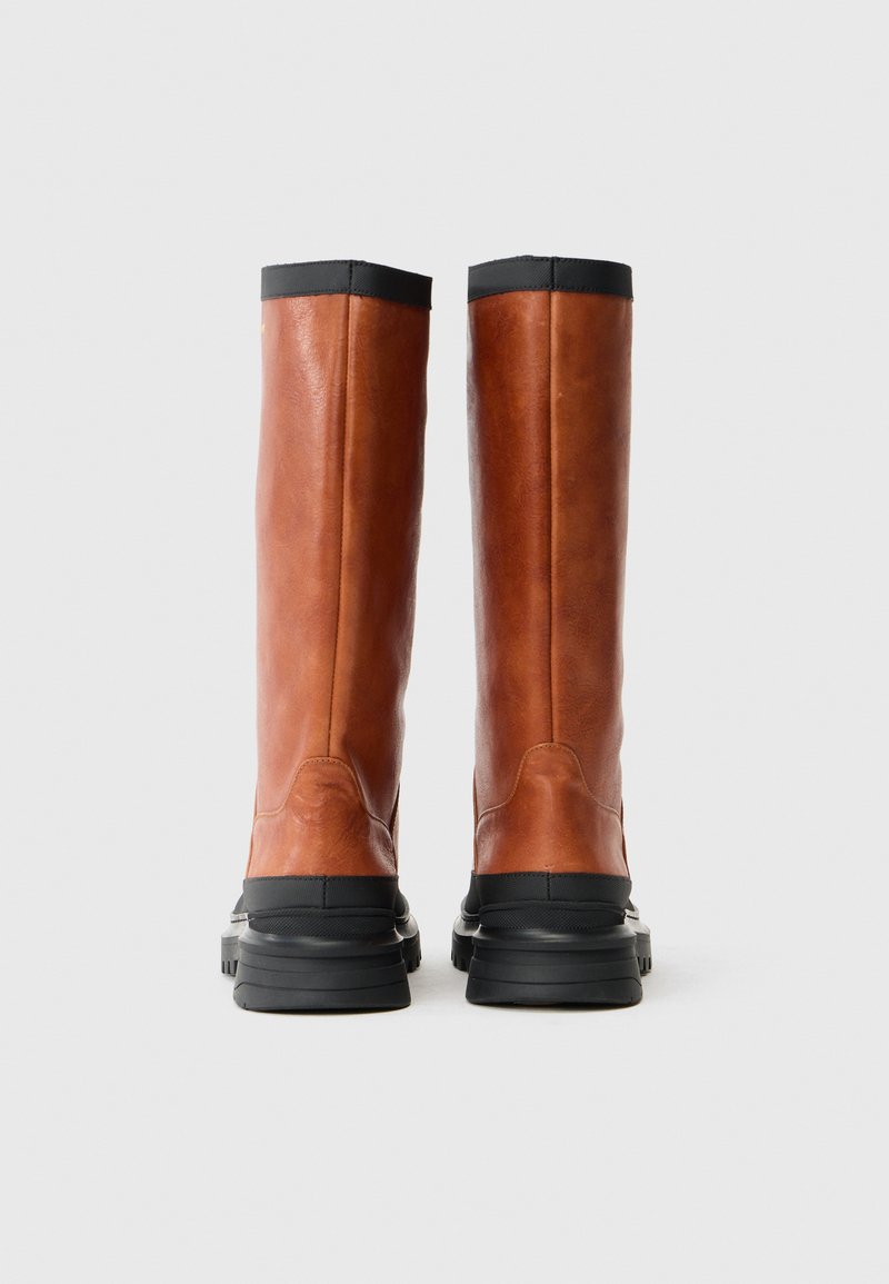 Stivali alti fino al ginocchio in pelle marrone con una finitura liscia, suole in gomma nera e un bordo superiore a contrasto nero, con semplici dettagli di cucitura.