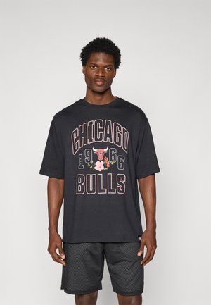 Black cotton t-shirt featuring "CHICAGO BULLS" text, a bull graphic, and floral accents. Short sleeves and relaxed fit. Paired with mesh shorts.