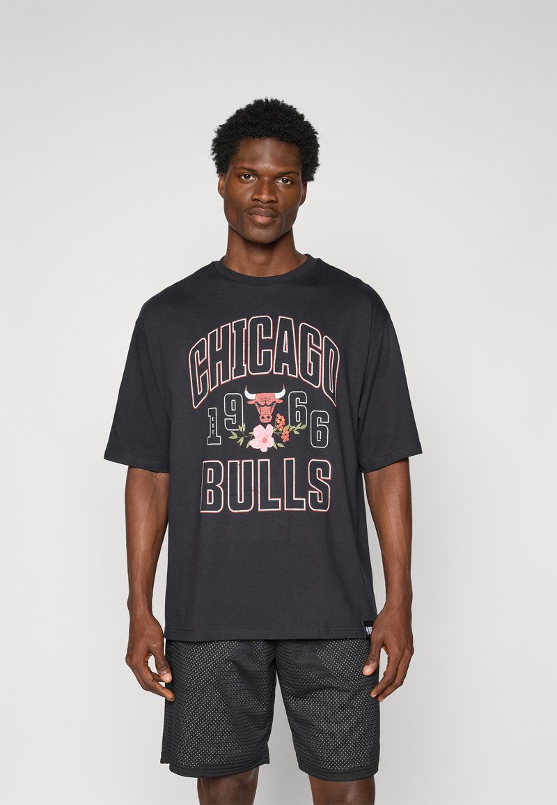 Črna bombažna majica s kratkimi rokavi, ki prikazuje napis "CHICAGO BULLS", grafiko bika in cvetlične detajle. Ohlapen kroj. Kombinirana z mrežastimi kratkimi hlačami.