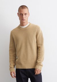 Beige gerippter Strickpullover mit rundem Halsausschnitt und langen Ärmeln, ausgestattet mit strukturiertem Stoff und einem taillierten Bündchen, kombiniert mit dunklem Denim.