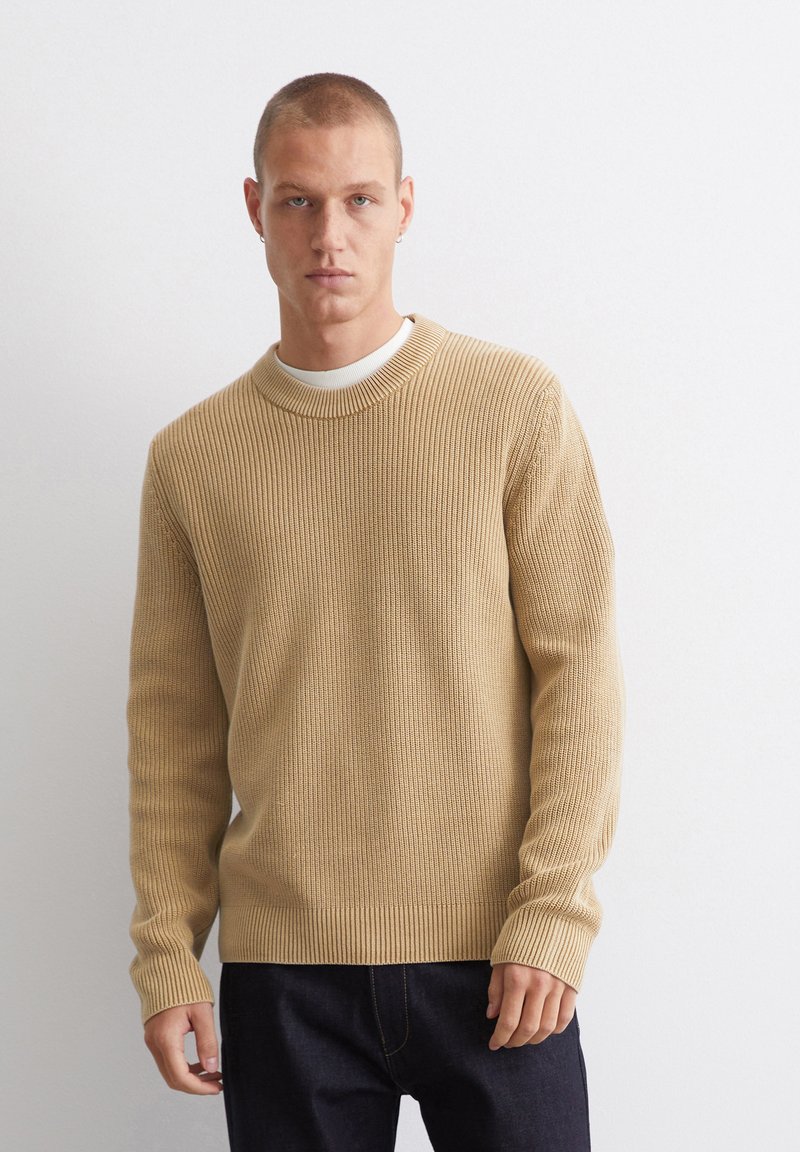 Beige gerippter Strickpullover mit rundem Halsausschnitt und langen Ärmeln, ausgestattet mit strukturiertem Stoff und einem taillierten Bündchen, kombiniert mit dunklem Denim.