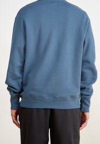 Blå sweatshirt av mjukt tyg, med ribbad fåll och muddar, en avslappnad passform och utan synliga logotyper eller mönster.