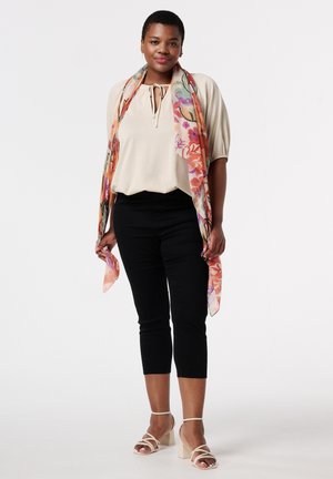 Haut beige avec un détail de nœud à l'avant, associé à un pantalon noir coupe crop et une écharpe pastel à motifs floraux. Sandales à talons blocs de couleur claire.