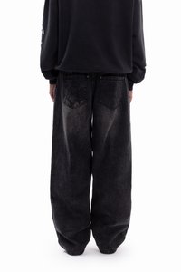 Black oversized denim pants with a faded texture, featuring two back pockets and loose-fitting design, paired with a black sweatshirt.