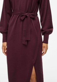 Bordo ilga rankovė su diržu liemens srityje, suteikianti šoninio skeltuko ir tekstūruoto audinio elementų. Lygus paviršius ir minkštas kritimas pabrėžia dizainą.