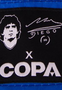 Zwarte patch met een geborduurd beeld van een persoon met kort haar, naast een handtekening en de tekst "COPA" in vet wit, tegen een blauwe achtergrond.