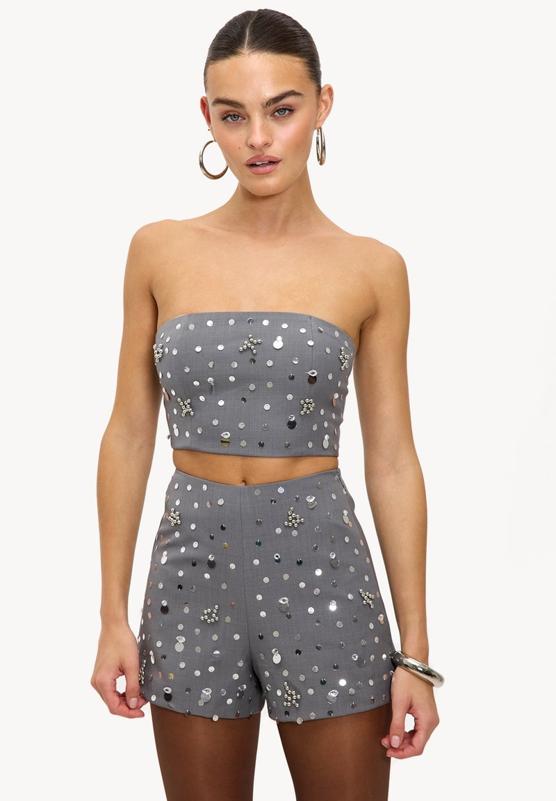 Femme portant un crop top gris sans bretelles et un short taille haute assorti, tous deux ornés de sequins argentés et de perles.