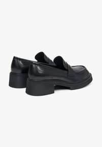 Zwarte lederen instappers met een ronde neus, platte gestapelde hak en minimale stiksels. Met een soepele structuur en een subtiele glans.