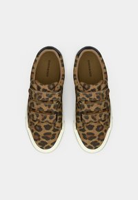 Pár hnedo-čiernych tenisiek s leopardím vzorom, vybavených tromi suchými zipsami a bielymi gumovými podrážkami na jednoduchom pozadí.