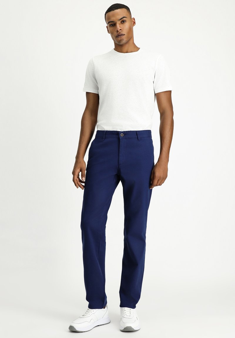 Pantaloni blu navy in misto cotone, con design a gamba dritta, chiusura con bottone e tasche. Abbinati a una t-shirt bianca a collo rotondo.