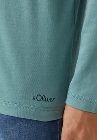 Turkusowa koszula z długim rękawem wykonana z miękkiego materiału, z wykończonym szwem i logo s.Oliver w granatowym kolorze w dolnej części.