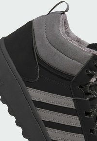 Zapatilla alta de color negro y gris con parte superior de ante y sintético, suela texturizada y franjas en contraste con acentos metálicos.