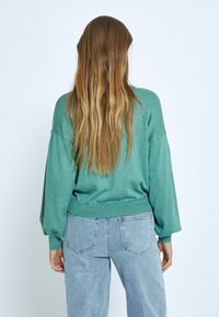 Mint green oversized sweater with long, balloon sleeves and ribbed hem, paired with high-waisted light blue jeans. Smooth texture.