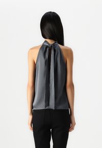 Haut halter gris avec une texture lisse, doté d'un nœud à l'arrière ; associé à un pantalon noir, mettant en valeur un design à dos nu.