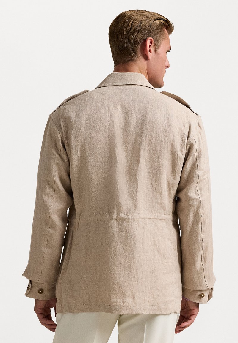 Veste en lin beige avec une coupe décontractée, dotée d'un col, d'épaules épaulettes et de poignets à boutons. Texture lisse avec un léger brillant.