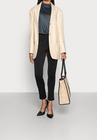 Beige blazer, svart åtsittande topp och smala svarta byxor; svarta spetsiga klackar och en texturerad tan toteväska med svarta accenter.